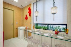 Na copa, cuba de chão com torneira de teto, mesa em vidro com quatro banquetas, parede de tijolinhos rústicos, pendentes de cristal, persianas Hunter Douglas e esculturas vermelhas de Marilene Ropelato. A janela recebeu floreiras com ervas e especiarias para saborizar águas e chás