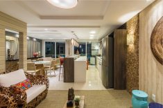 O descontraído estar integrado com hall de entrada ganhou tapete de fibras (Yellowart), mesa de centro rústica com vidro (Raffinatto), dupla de poltronas de fibra natural da Mellie. Nas paredes, papel de parede tipo folhagem e listrado (Spengler Decor), e pastilhas de coco (Pastilhart).