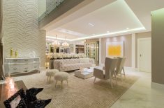 O pé-direito amplo é realçado pela parede com textura em quartzo assinada pela artista plástica Marilene Ropelato. Rasgos estratégicos no gesso, com fitas de LED embutidas, garantem iluminação cênica indireta